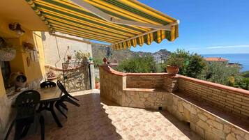 Un balcon avec un mur en pierre, une table avec des chaises et un auvent jaune à rayures.