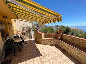 Ein Balkon mit einer Steinmauer, einem Tisch und Stühlen sowie einem gelb gestreiften Markisenvorzelt.