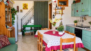 Zona pranzo con tavolo apparecchiato per quattro, un divano verde e una cucina con mobili color petrolio.
