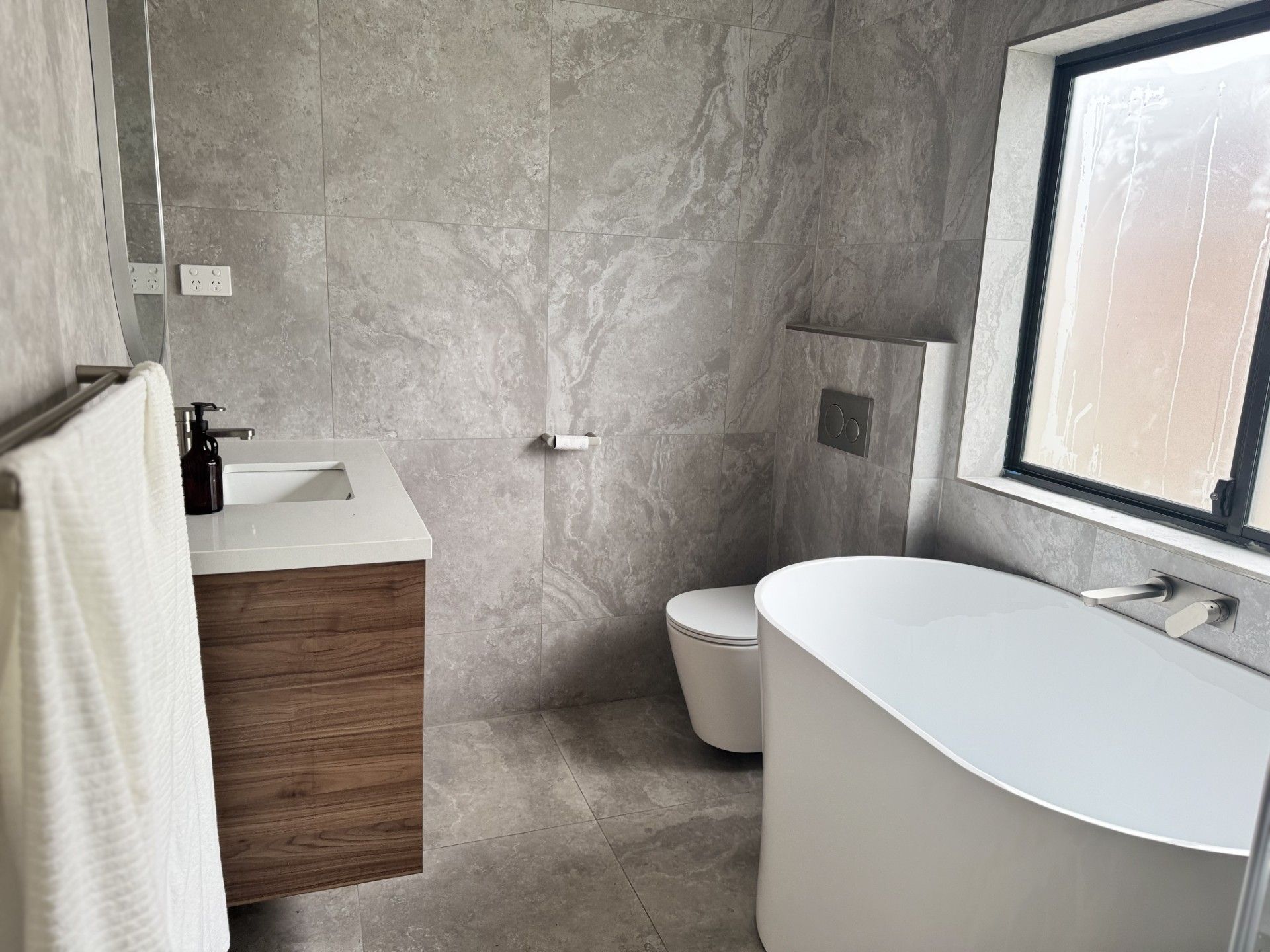 A modern bathroom with a freestanding bathtub, a toilet, and a vanity with a mirror.