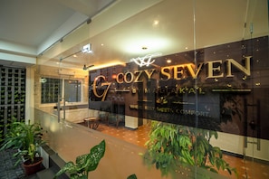 Un interior moderno con una pared de vidrio que muestra el nombre 'COZY SEVEN' y un letrero que indica un restaurante.