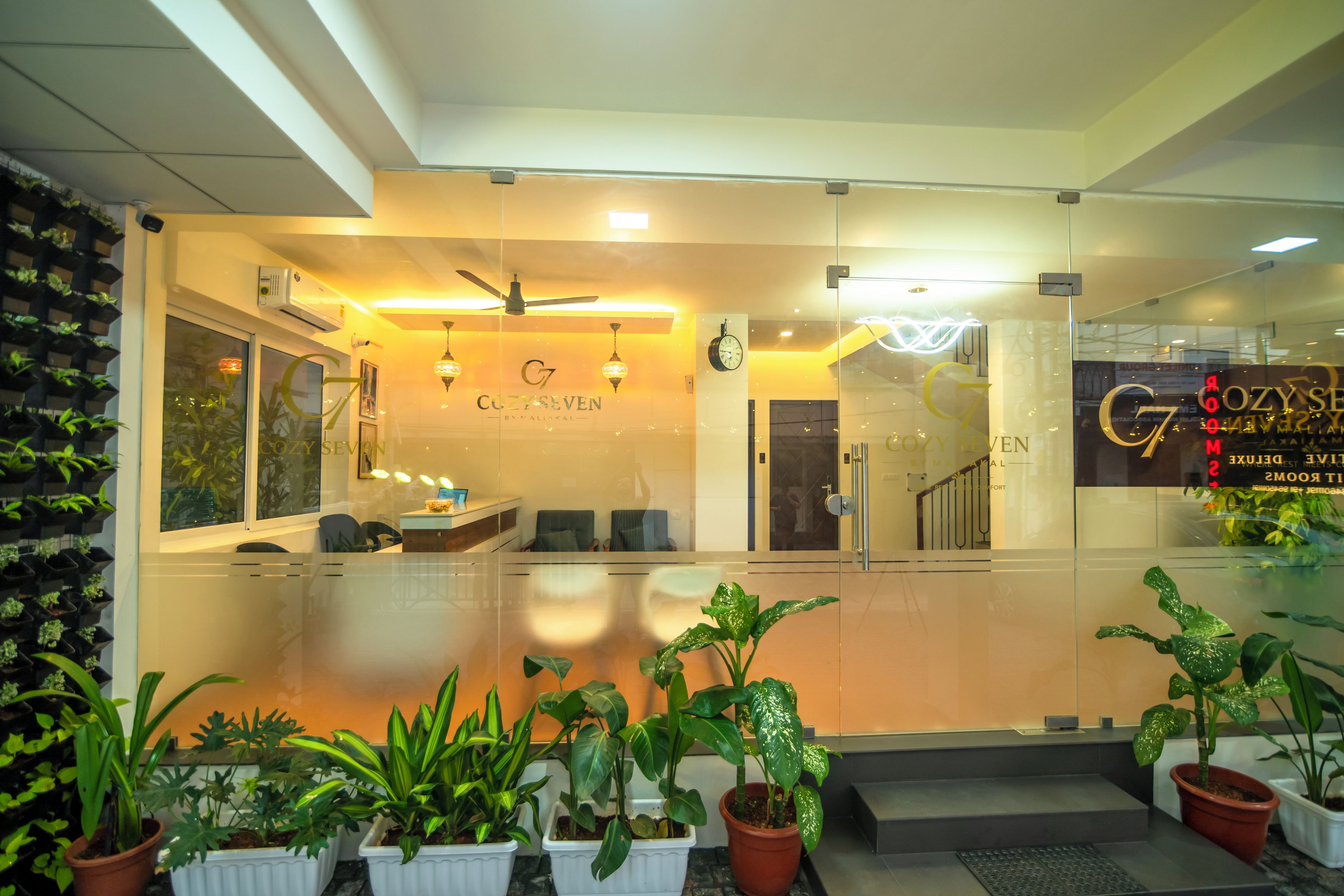 A reception area with a glass partition, a reception desk, seating, and potted plants.