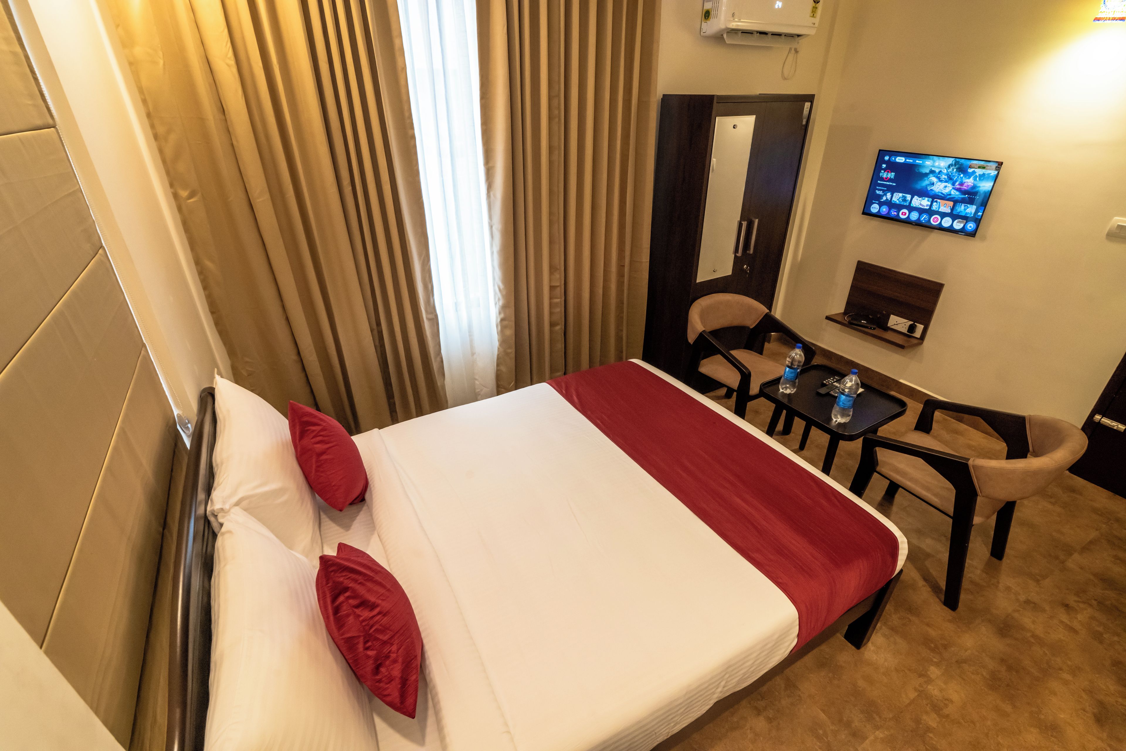 Habitación de hotel con cama, escritorio, silla, televisor y ventana con cortinas.