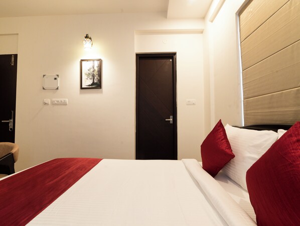 A hotel room with a bed, a door, a wall-mounted light, and a power outlet. - Cozy Seven - 50m to North Railway Station (Kanayannur)