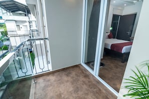 A balcony with a glass door leading to a bedroom with a bed and a red pillow. - Cozy Seven - 50m to North Railway Station (Kanayannur)