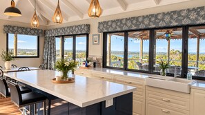 A modern kitchen with a large island, white cabinetry, and large windows offering a view of the landscape. - Gracie & Dan’s Coastal Retreat | Lake Views | Sleeps 5, 2Bath| Golf & Beach Walk (Preston Beach)
