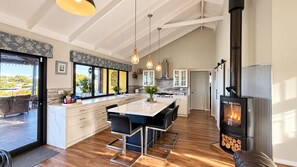 A modern kitchen with a central island, a wood-burning stove, and a view of the outdoors. - Gracie & Dan’s Coastal Retreat | Lake Views | Sleeps 5, 2Bath| Golf & Beach Walk (Preston Beach)