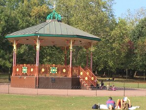 Ein Pavillon mit Dach und Geländern, umgeben von einem Zaun, in einer Parkanlage.