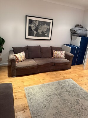 Ein Wohnzimmer mit einem braunen Sofa, einem gemusterten Teppich und einer gerahmten Weltkarte an der Wand.