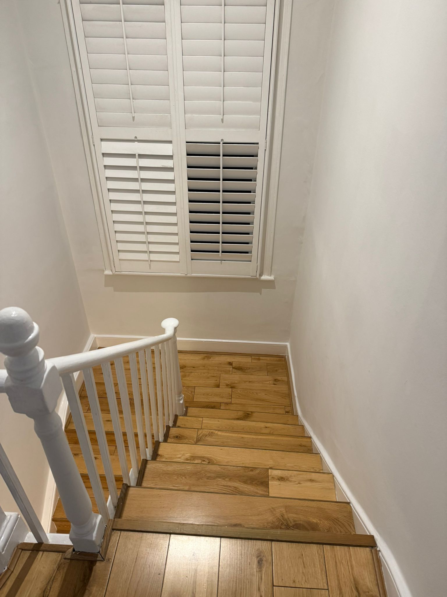 Un escalier en bois avec des rampes blanches et une fenêtre avec des volets blancs.