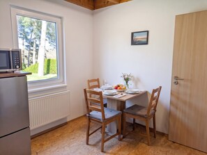 A dining area with a table set for two, a microwave, and a view of trees through a window. - Ferienhaus Fünfseen-Glück (Fünfseen)