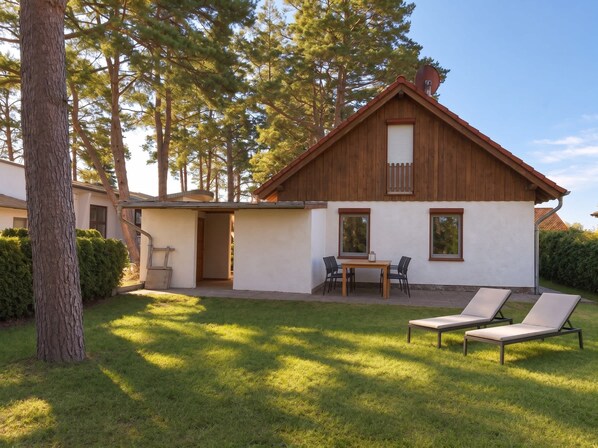 A house with a wooden exterior, a patio with a table and chairs, and a lawn.