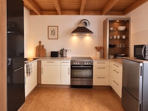 A modern kitchen with a built-in oven, a coffee maker, and a wooden ceiling. - Ferienhaus Fünfseen-Glück (Fünfseen)