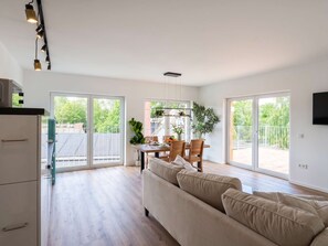 Amplia sala de estar con sofá, mesa de comedor, sillas, ventanas grandes y una cocina con armarios y encimera.