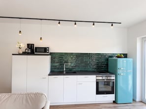 Una cocina moderna con encimera negra, armarios blancos, salpicadero verde y refrigerador aguamarina.