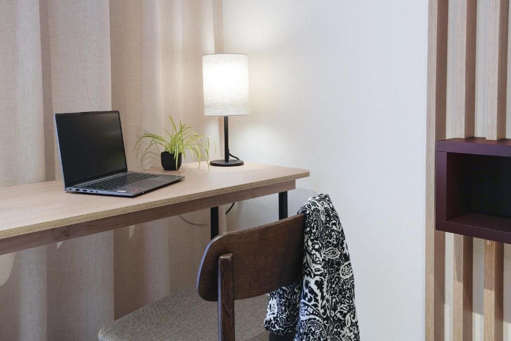 Un ordinateur portable est posé sur un bureau en bois, avec une lampe et une plante en pot à côté.