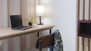 Un ordinateur portable est posé sur un bureau en bois, avec une lampe et une plante en pot à côté.