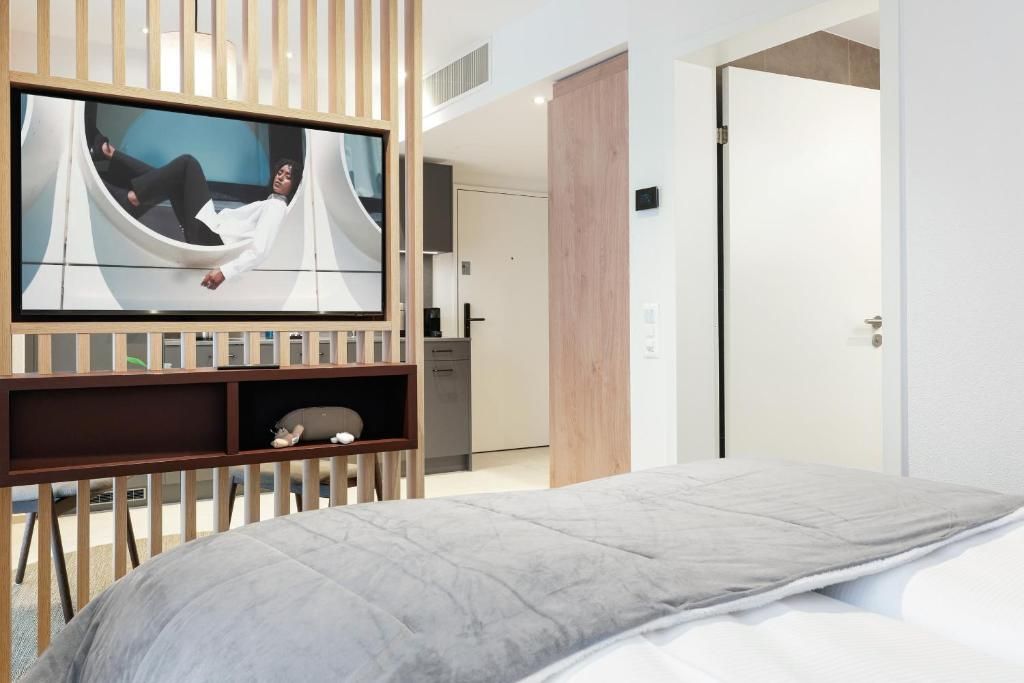 Habitación de hotel moderna con cama, televisor montado en un panel de madera y vista hacia la habitación contigua.