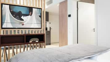 Habitación de hotel moderna con cama, televisor montado en un panel de madera y vista hacia la habitación contigua.