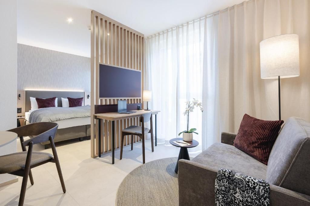A modern hotel room with a bed, a desk, a sofa, and a TV.