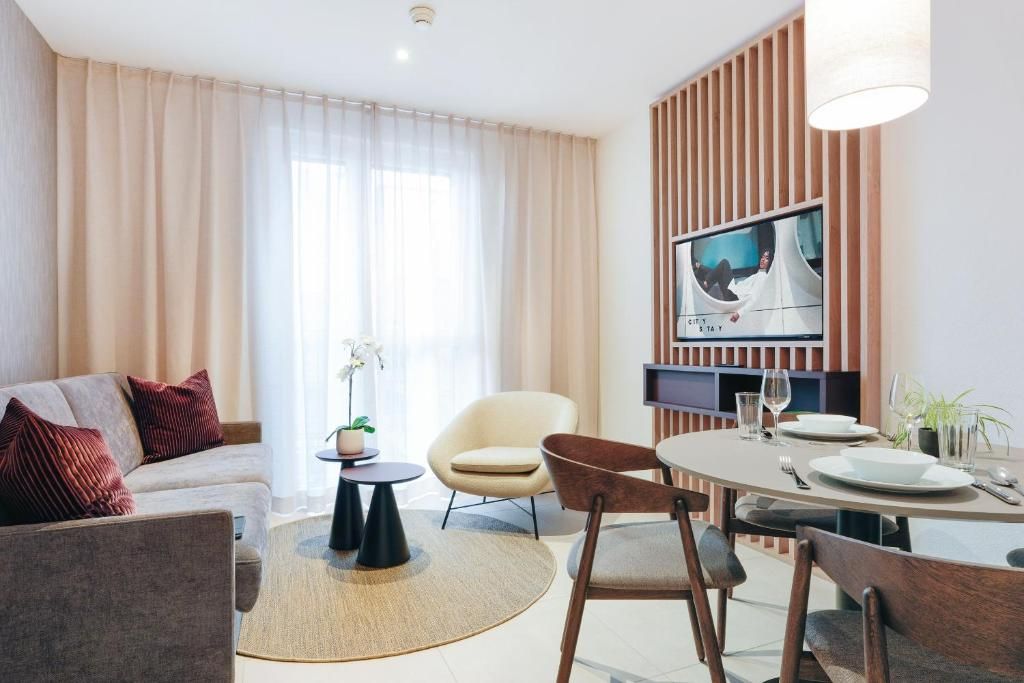 Una sala moderna con sofá, sillas, una mesa de comedor para dos personas y un televisor montado en una pared de paneles de madera.
