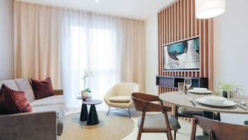 Una sala moderna con sofá, sillas, una mesa de comedor para dos personas y un televisor montado en una pared de paneles de madera.