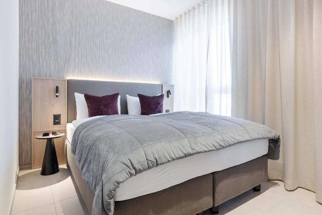Een moderne hotelkamer met een groot bed, nachtkastjes en een hoofdbord met ingebouwde verlichting.