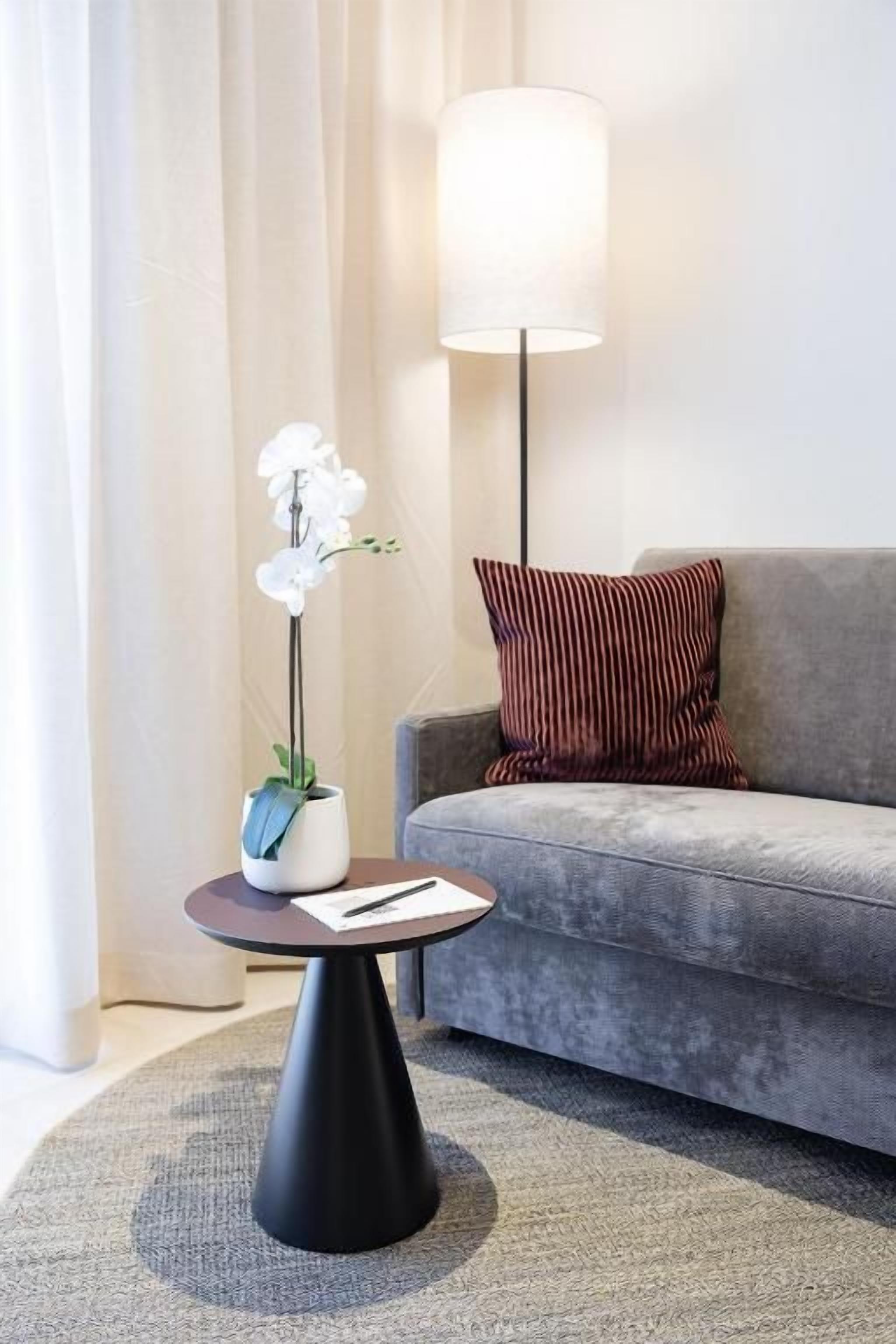 Ein modernes Wohnzimmer mit einem grauen Sofa, einem runden schwarzen Couchtisch, einer weißen Orchideenpflanze und einer Stehlampe.