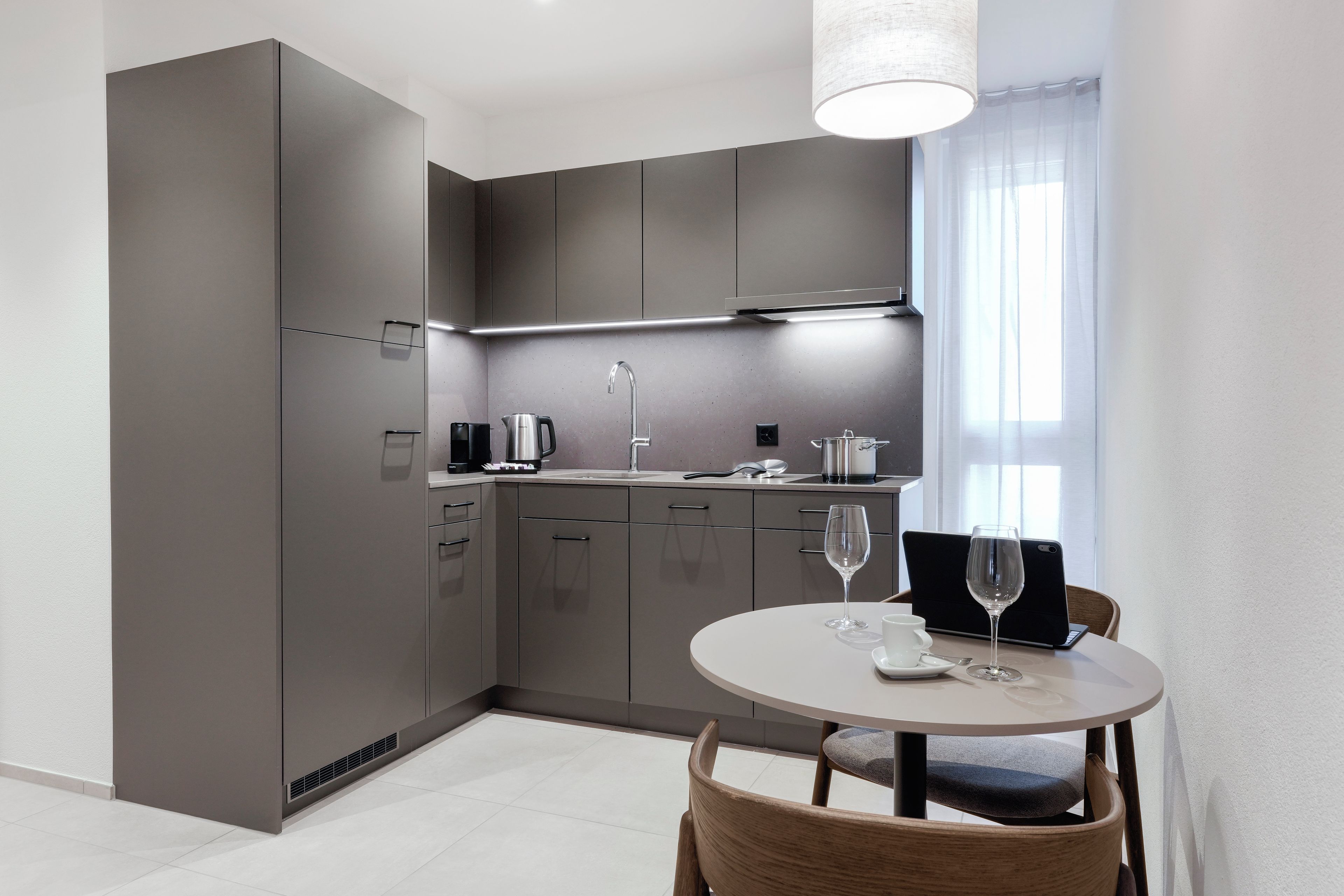 Una cocina moderna con armarios grises, una mesa redonda y una ventana con cortinas de gasa.