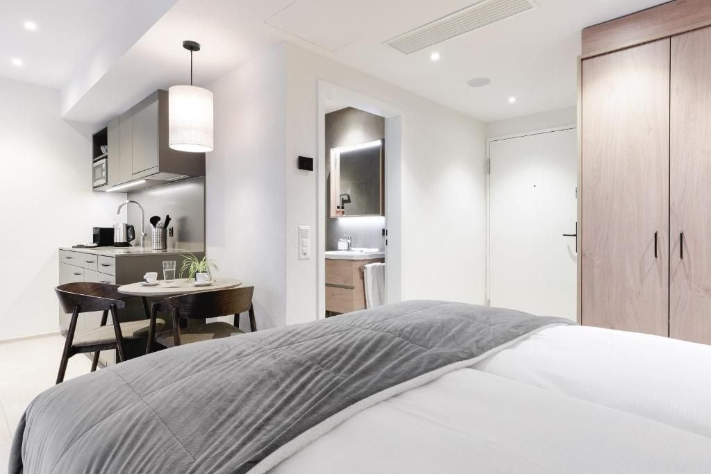 A modern bedroom with a bed, a desk, and a chair. There is a wardrobe and a mirror in the room.