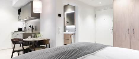 A modern bedroom with a bed, a desk, and a chair. There is a wardrobe and a mirror in the room.