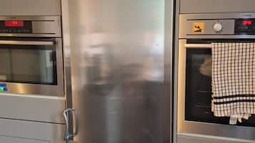 Frigorifero in acciaio inossidabile con doppie ante e display digitale, posizionato tra un forno a microonde e una lavatrice in una cucina.