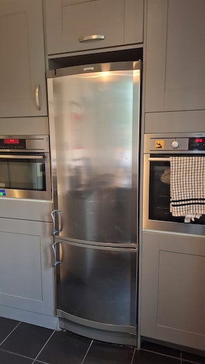 A stainless steel double-door refrigerator with a digital display, situated between a microwave and a washing machine in a kitchen. - Stunning apartment in the heart of Hampstead (London)