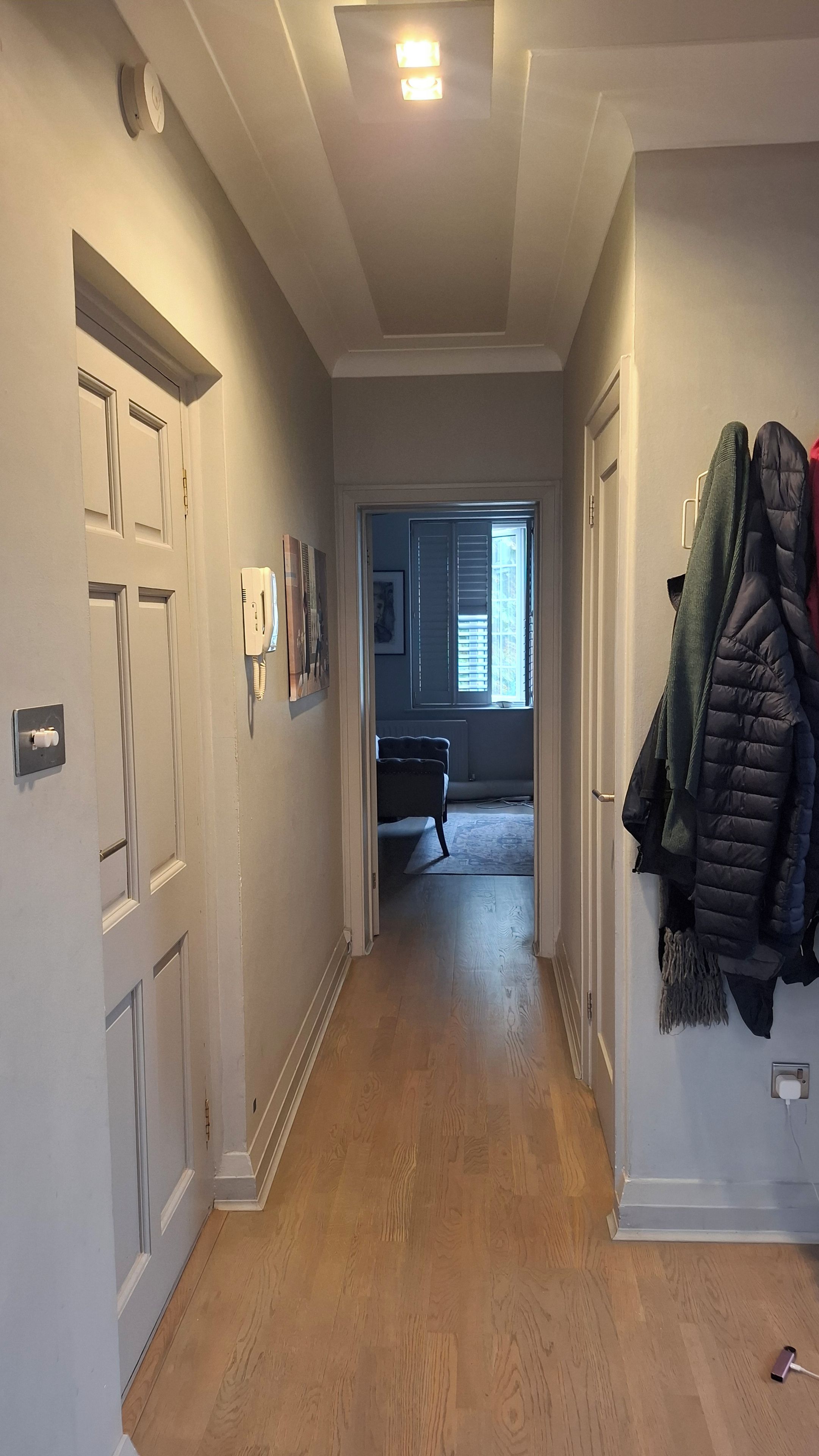 A hallway with wooden flooring, white walls, and a door on the left.
