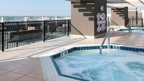 Een zwembad op het dak met een jacuzzi, een glazen hekwerk en uitzicht op de skyline.