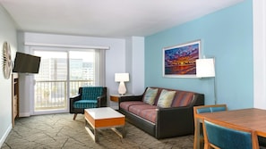 Ein Hotelzimmer mit Sofa, Sessel, Esstisch und einem Gemälde an der Wand.