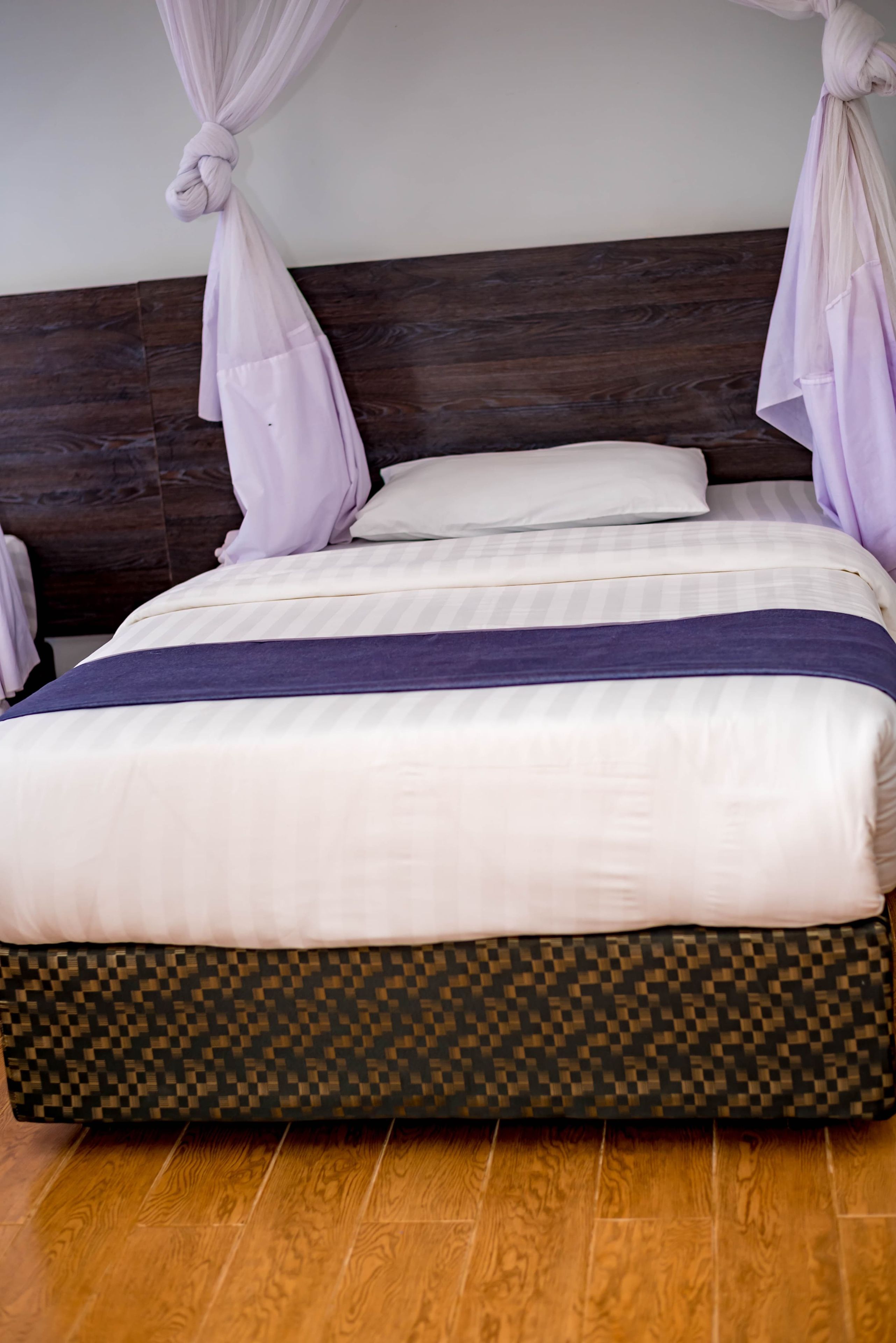 Una cama con cabecera oscura, ropa de cama blanca y falda estampada.
