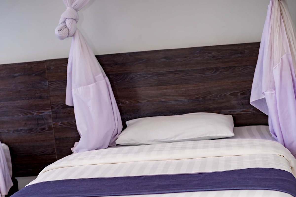 A bed with a dark headboard, white bedding, and a patterned bed skirt.