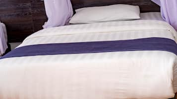 Una cama con cabecera oscura, ropa de cama blanca y falda estampada.