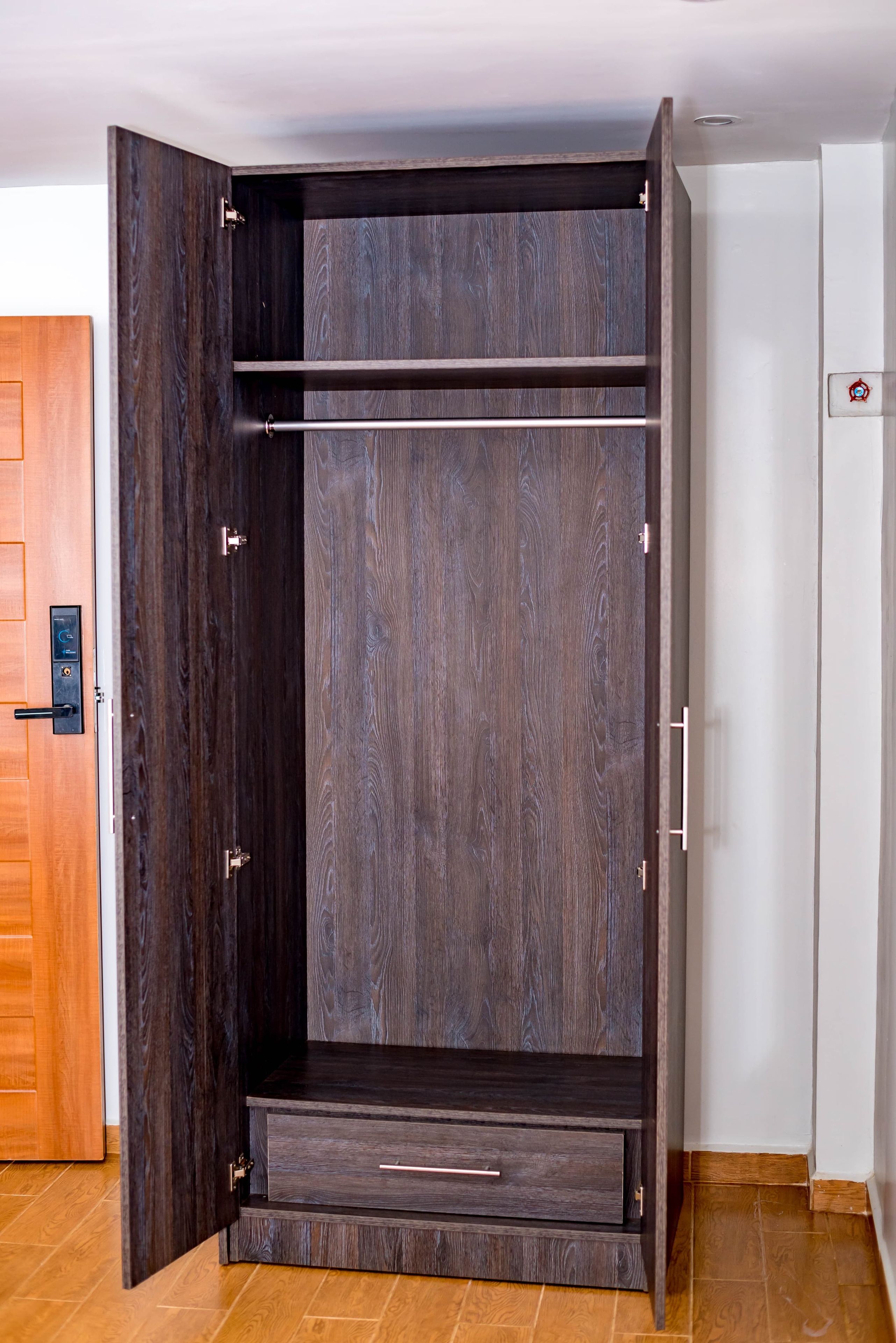 Un armario con acabado en madera oscura, puerta corredera y un cajón pequeño.