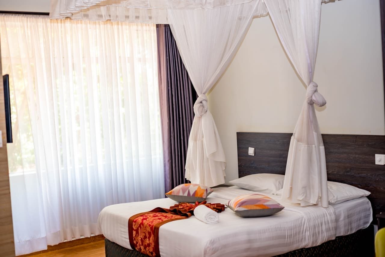 Habitación de hotel con cama, dosel, ventana con cortinas y vista al exterior.