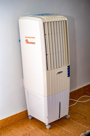 Un radiateur portatif blanc, doté d’un panneau de commande, est posé sur un plancher en bois, contre un mur uni.