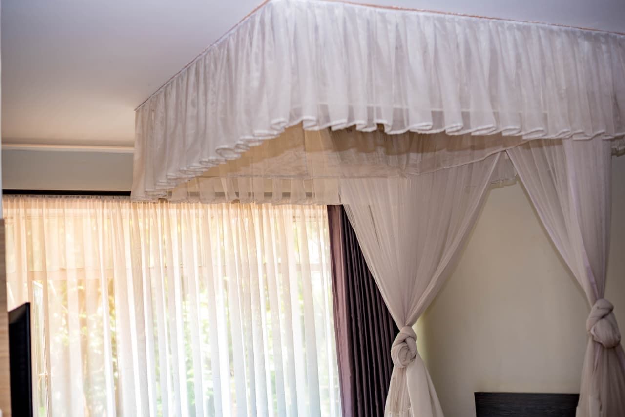 Una habitación con cama a dosel, una ventana con cortinas translúcidas y vistas al exterior con vegetación.