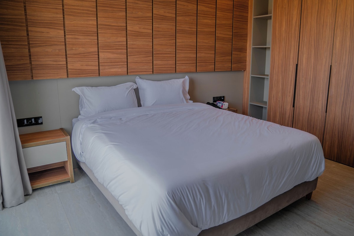 Una cama bien hecha con sábanas blancas en una habitación moderna con paneles de madera en las paredes y un armario de madera.