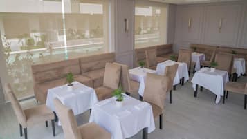 A restaurant with beige sofas and white tables, large windows, and a view of the outside.