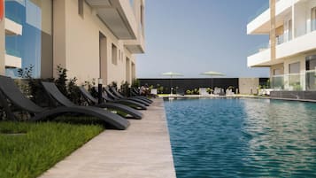 A swimming pool with lounge chairs and umbrellas, surrounded by a building with a modern design.