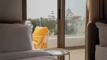 A hotel room with a bed, a chair with a yellow cushion, and a view of the outside through large windows.