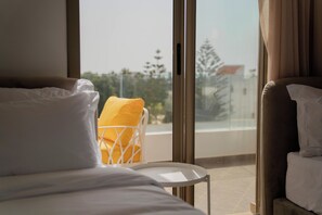 Habitación de hotel con una cama, un sillón con cojín amarillo y vistas al exterior a través de amplias ventanas.