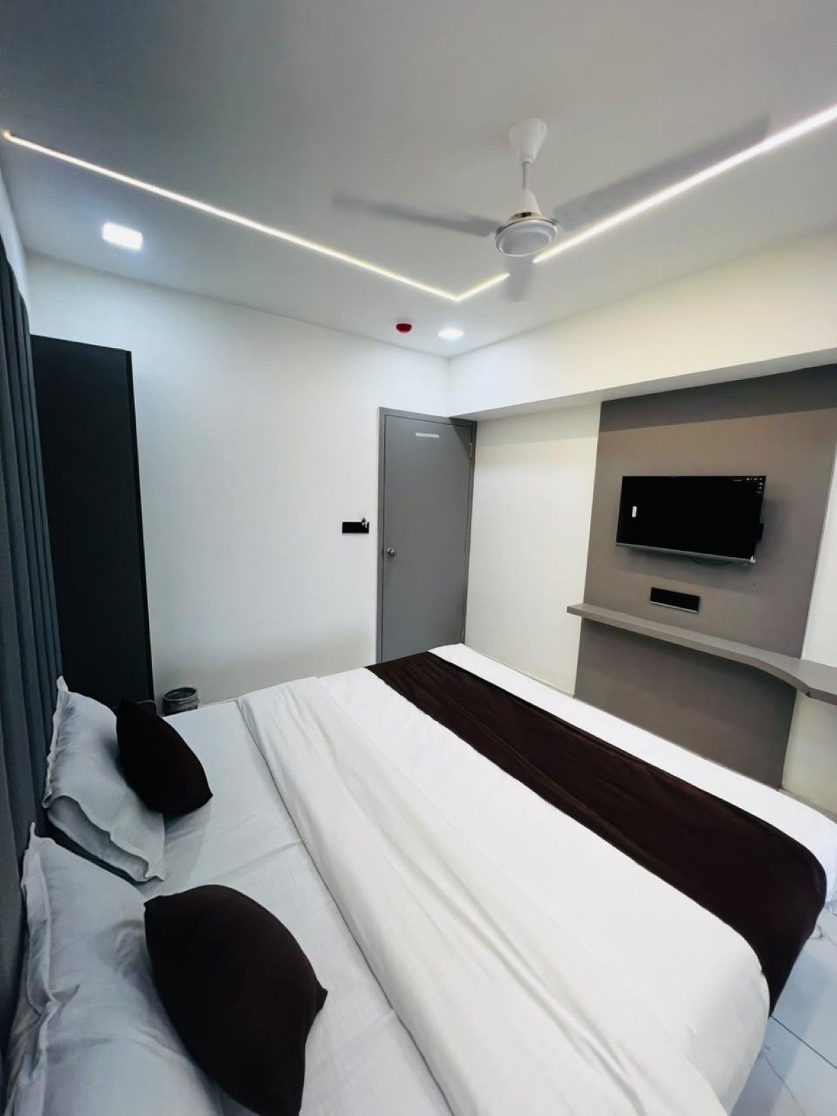 Quarto de hotel moderno com cama, TV de tela plana na parede, ventilador de teto e porta.