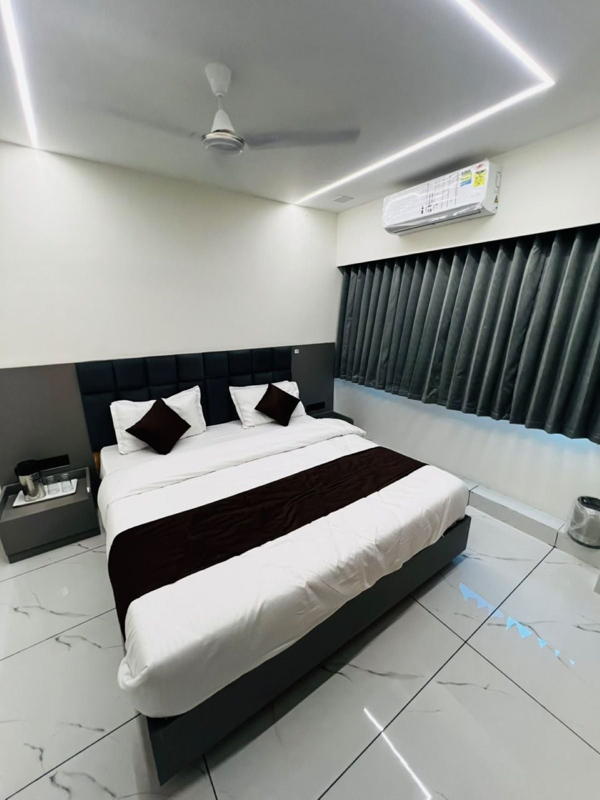 A modern bedroom with a large bed, a ceiling fan, an air conditioning unit, and a window with blinds.
